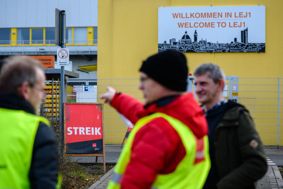 LEIPZIG, GERMANY - DECEMBER 17: Striking workers of an Amazon warehouse stand outside the facility on the first day of their strike on December 17, 2018 in Leipzig, Germany. Workers at two Amazon warehouses in Germany have gone on strike today in a long-standing dispute between the ver.di labor union and Amazon. For five years ver.di has demanded Amazon workers be paid according to wage models for the retail sector. Amazon classifies its warehouse workforce in Germany under logistics, which is a lower wage category. (Photo by Jens Schlueter/Getty Images)