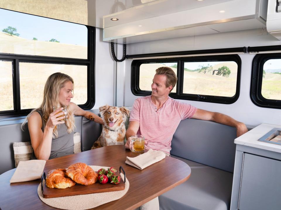 Two people and a dog sitting at a dining table surrounded by windows.