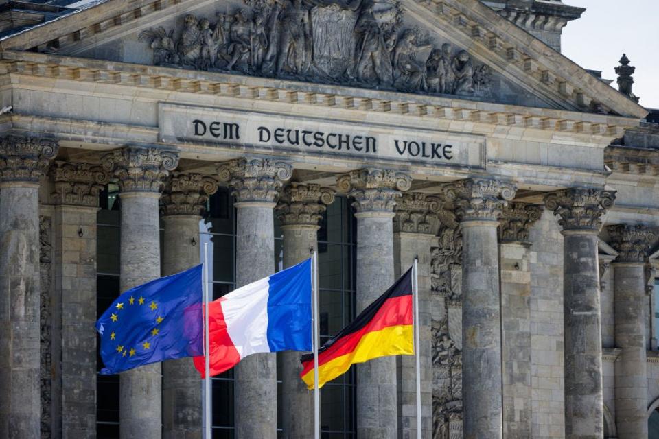 EU, French, and German flags flutter in front of the Reichstag building housing the Bundestag