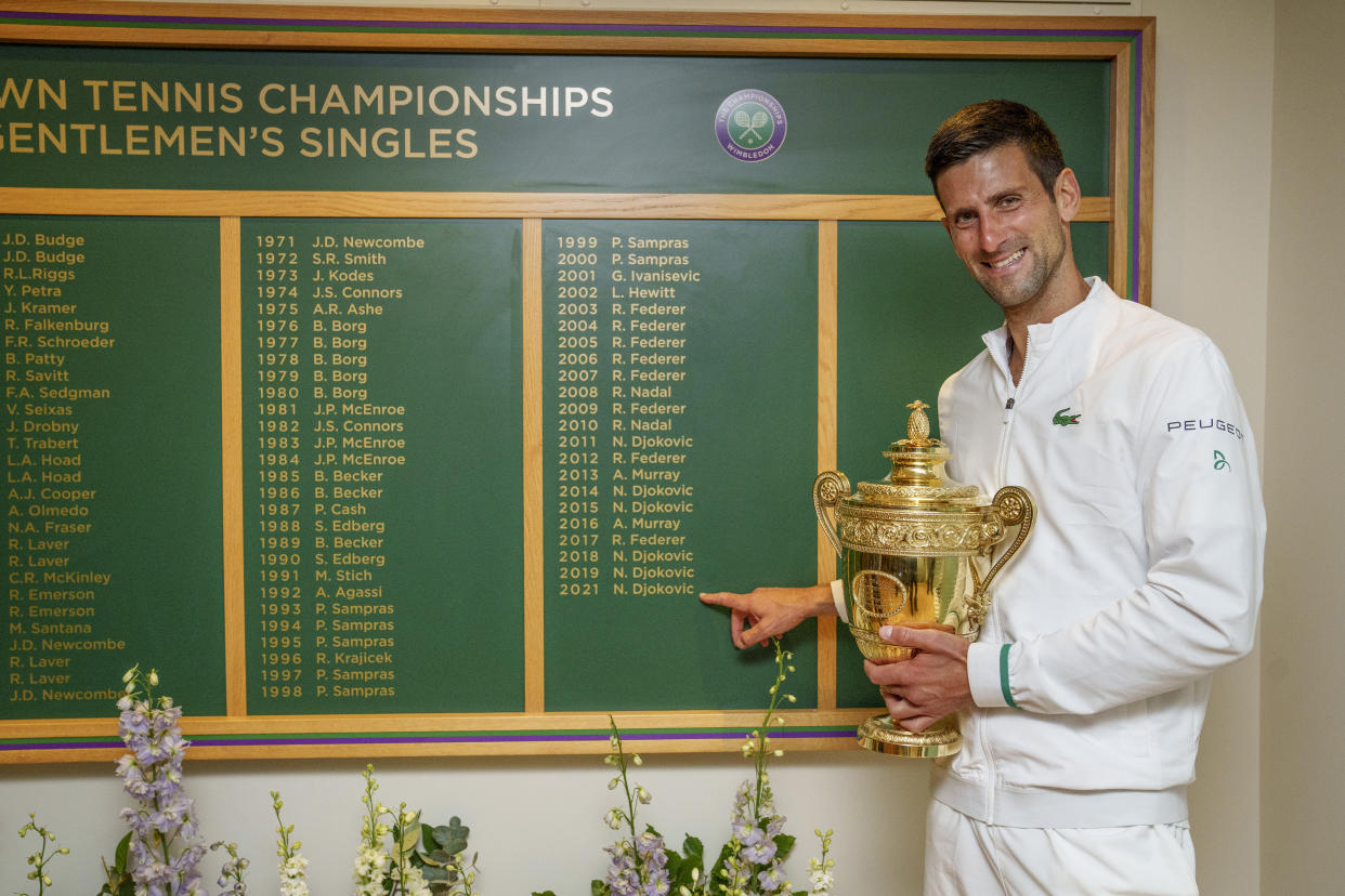 LONDON, ENGLAND - JULY 11: Novak Djokovic of Serbia celebrates with the trophy  in front of the honours board and points to his name after winning his men's Singles Final match against Matteo Berrettini of Italy on Day Thirteen of The Championships - Wimbledon 2021 at All England Lawn Tennis and Croquet Club on July 11, 2021 in London, England. (Photo by AELTC/Thomas Lovelock - Pool/Getty Images)