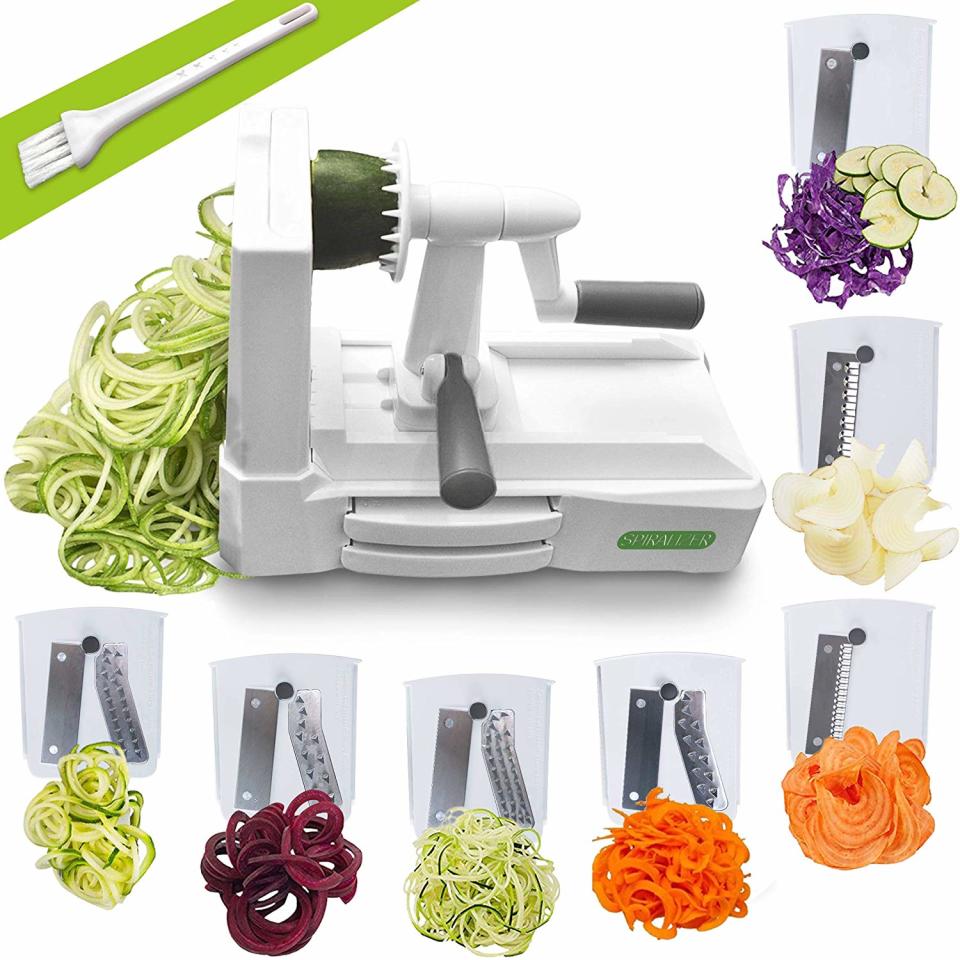 a spiralizer and its seven attachments with several vegetables cut up on a white background