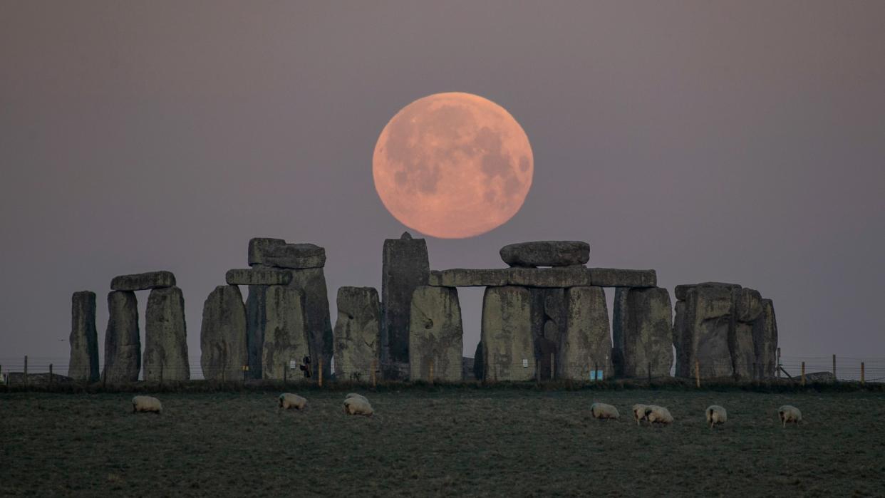  The full moon hangs in the sky above a monument consisting of stacked rock slabs. 