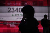 People wearing face masks walk past a bank electronic board showing the Hong Kong share index at Hong Kong Stock Exchange Monday, April 6, 2020. Asian shares and U.S. futures have rebounded as investors grasped at threads of hope that the battle against the coronavirus pandemic may be making some progress in some hard-hit areas.(AP Photo/Vincent Yu)