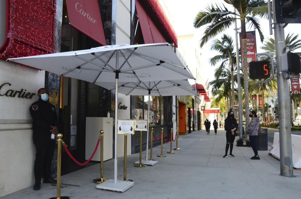 A security guard in a face mask stands outside Cartier jewelry shop with no customers on line during the coronavirus pandemic on Rodeo Drive, Thursday, Dec. 3, 2020, in Beverly Hills, Calif. The new stay-at-home order will last at least three weeks, cutting sharply into the most profitable shopping season and threatening financial ruin for businesses already struggling after 10 months of on-again, off-again restrictions and slow sales because of the pandemic. (AP Photo/Pamela Hassell)