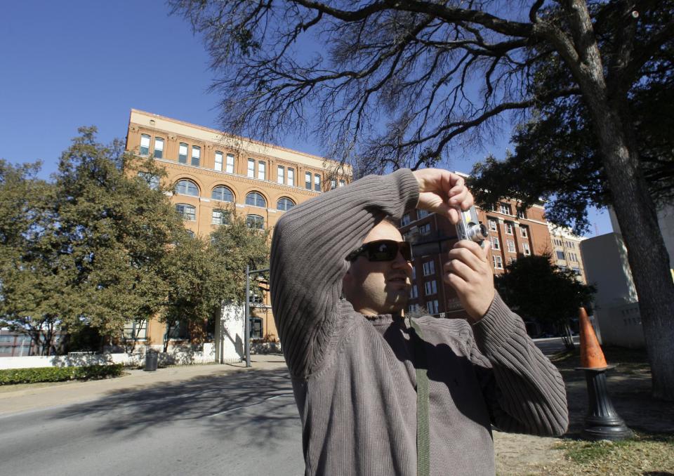 FILE - In this Jan. 5, 2011 photo, Rafael Boff, of Brazil, takes photographs while visiting Dealey Plaza, site of president John F. Kennedy's assassination, in Dallas. The building once used as a book depository is seen in the background. Three cities loom large in the life and death of John F. Kennedy: Washington, D.C., where he served as U.S. president and as a senator; Dallas, where he died, and Boston, where he was born. With the 50th anniversary of his Nov. 22, 1963 assassination at hand, all three places are worth visiting to learn more about him or to honor his legacy. (AP Photo/Tony Gutierrez)