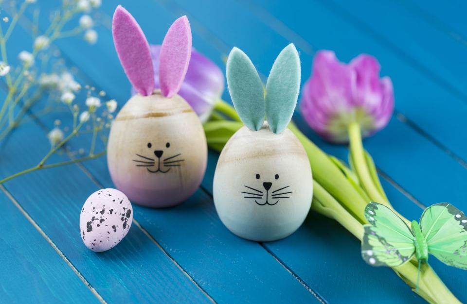 wooden easter eggs with mini bunny ears and bunny faces next to flowers and a butterfly