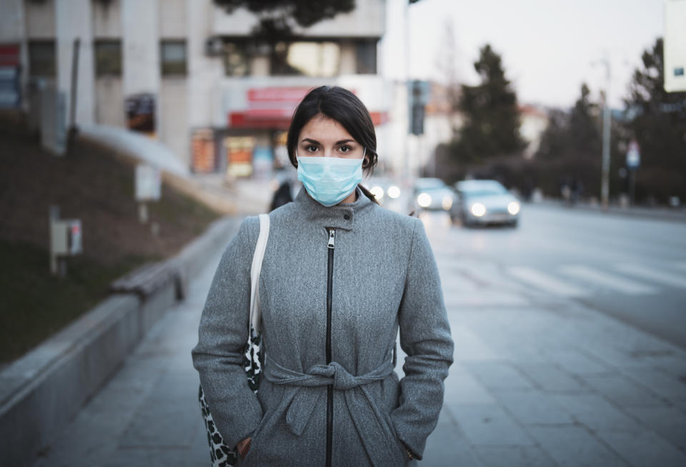 Portrait of young Latino woman with face mask on the street, looking at camera.