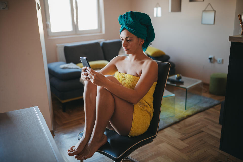 A woman in her living room in a bath towel using her phone