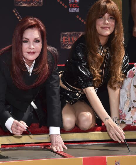 Two women lean over cement to sign it.