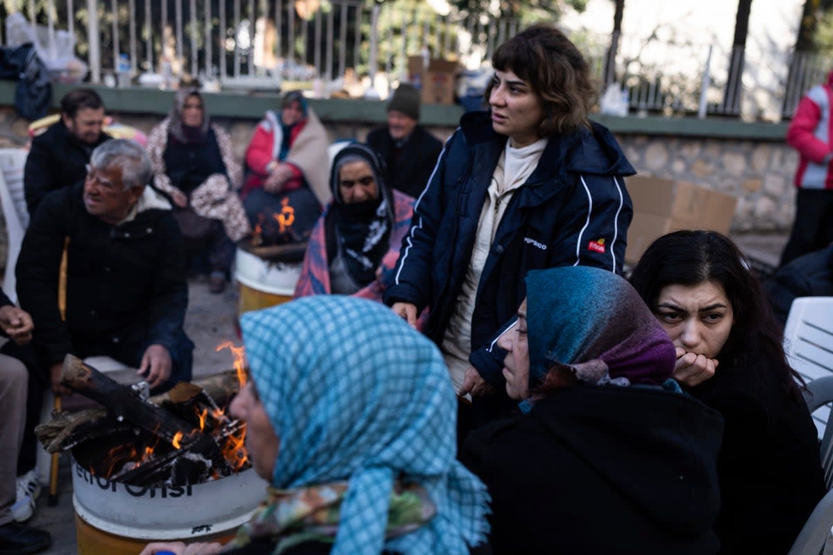 Locals sit around bonfire as firefighters and rescue teams search for people in a destroyed building, in Adana, southern Turkey (Copyright 2023 The Associated Press. All rights reserved)