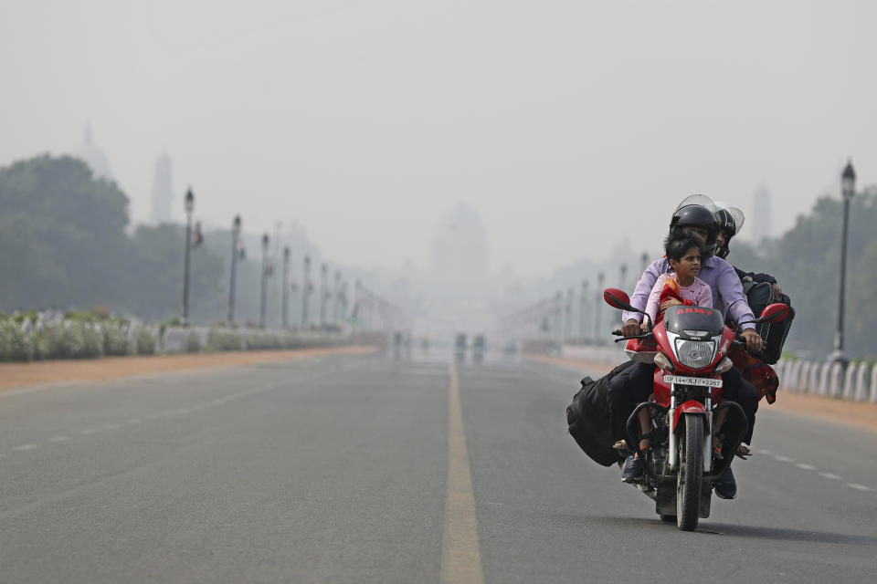 India's Presidential Palace, in the backdrop, is covered with smog as a family rides a motorbike on Rajpath, the ceremonial boulevard, in New Delhi, India, Tuesday, Nov. 19, 2019. India's Parliament has discussed the toxic air threatening the lives of the capital region's 48 million people, with opposition leaders demanding the creation of a parliamentary panel to remedy the situation on a long-term basis. (AP Photo/Altaf Qadri)