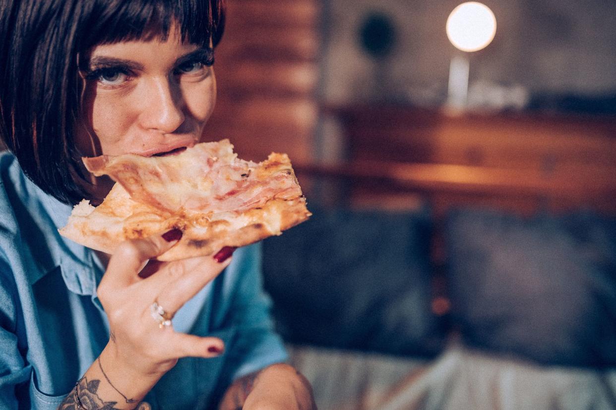 Lonely tattooed woman eating pizza in bed