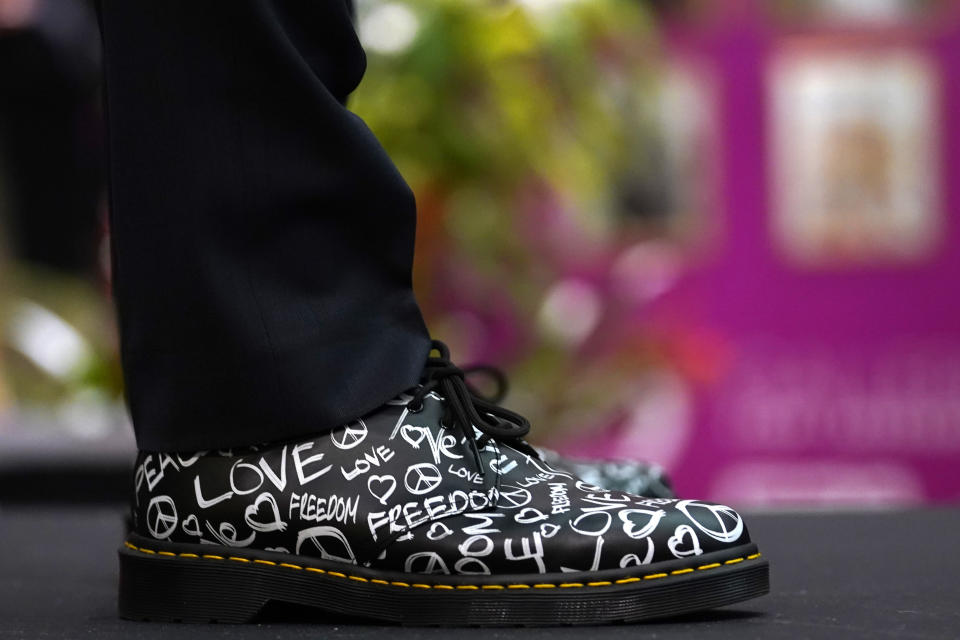 A speaker wears shoes advocating for love, peace and freedom during the opening reception of "Take PRIDE! A Retrospective of LGBTQ+ Life in South Florida" exhibit, Wednesday, May 31, 2023, in Fort Lauderdale, Fla. (AP Photo/Lynne Sladky)