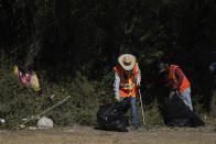 Men clean up items left behind by migrants near a dam along the Rio Grande, where migrants, many from Haiti, had been crossing, Thursday, Sept. 23, 2021, in Del Rio, Texas. The “amistad,” or friendship, that Del Rio, Texas, and Ciudad Acuña, Mexico, celebrate with a festival each year has been important in helping them deal with the challenges from a migrant camp that shut down the border bridge between the two communities for more than a week. Federal officials announced the border crossing would reopen to passenger traffic late Saturday afternoon and to cargo traffic on Monday. (AP Photo/Julio Cortez)