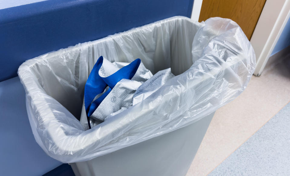 A trash can containing disposed blue and white medical items, located in a clinical or hospital setting