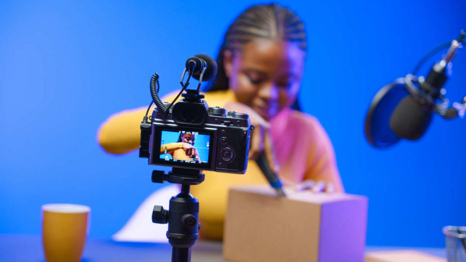 A dark-skinned vlogger girl in her studio starts unpacking a cardboard box. The blogger girl tells how convenient and easy it is to make orders in online stores. Unpacking a cardboard box, she tells about how quickly the goods were delivered to her from the online store.