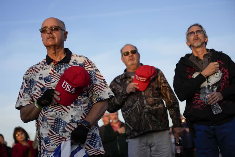 Simpatizantes del ex presidente de Estados Unidos Donald Trump se ponen de pie para el juramento a la bandera mientras esperan su llegada para un mitin en el Aeropuerto Internacional de Dayton el 7 de noviembre de 2022 en Vandalia, Ohio.