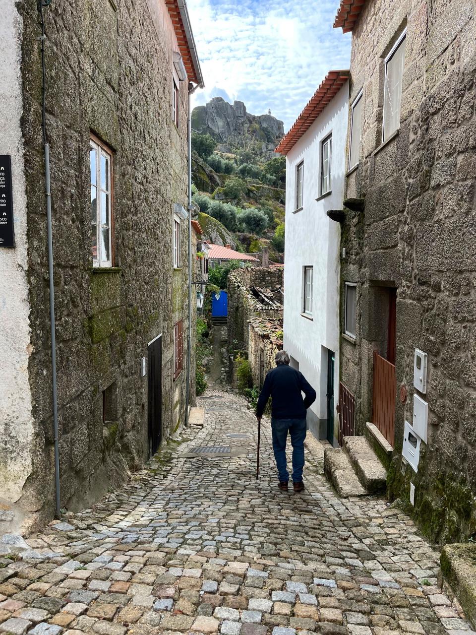 A man with a cane walks down a steep, narrow street in the boulder-strewn mountaintop village of Monsanto, Portugal on Sept. 18, 2023. (Kristen de Groot via AP)