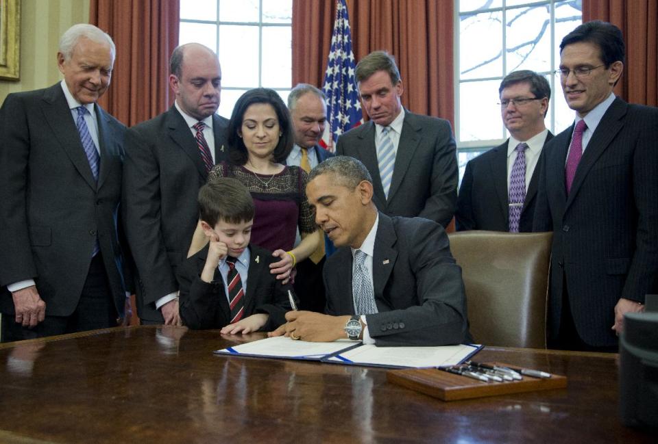 President Barack Obama signs the Gabriella Miller Kids First Research Act, Thursday, April 3, 2014, in the Oval Office of the White House in Washington. From left are, Sen. Orrin Hatch, R-Utah, Mark Miller, Ellyn Miller, and their son Jake, Sen. Timothy Kaine, D-Va., Sen. Mark Warner, D-Va., Mike Gillette, and House Majority Leader Eric Cantor of Va. (AP Photo/Manuel Balce Ceneta)