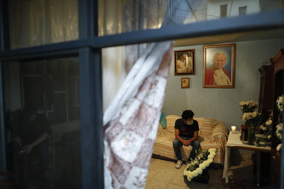 Hector Briseno grieves in front of the urn containing the ashes of his grandfather, Manuel Briseno Espino, 78, who died from complications due to COVID-19, in the Iztapalapa district of Mexico City, Wednesday, April 22, 2020. Due to social distancing restrictions, the seven family members from three generations who lived with him marked his passing with quiet prayers at home, unable to invite his many friends or other relatives, or to bury him in the cemetery plot with his late wife of 49 years, Consuelo Garcia Rodriguez. (AP Photo/Rebecca Blackwell)