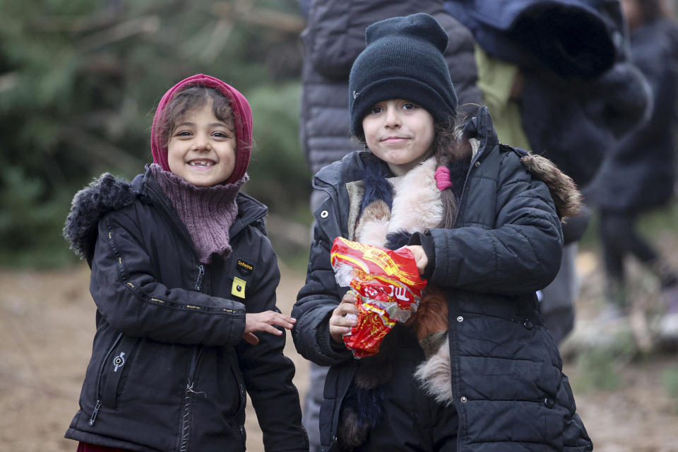 Migrant children eat chips as other migrants gather at the Belarus-Poland border near Grodno, Belarus, Saturday, Nov. 13, 2021. A large number of migrants are in a makeshift camp on the Belarusian side of the border in frigid conditions. Belarusian state news agency Belta reported that Lukashenko on Saturday ordered the military to set up tents at the border where food and other humanitarian aid can be gathered and distributed to the migrants. (Leonid Shcheglov/BelTA pool photo via AP)