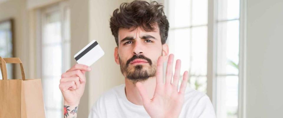 Young man eating asian sushi from home delivery using credit card as payment with open hand doing stop sign with serious and confident expression, defense gesture