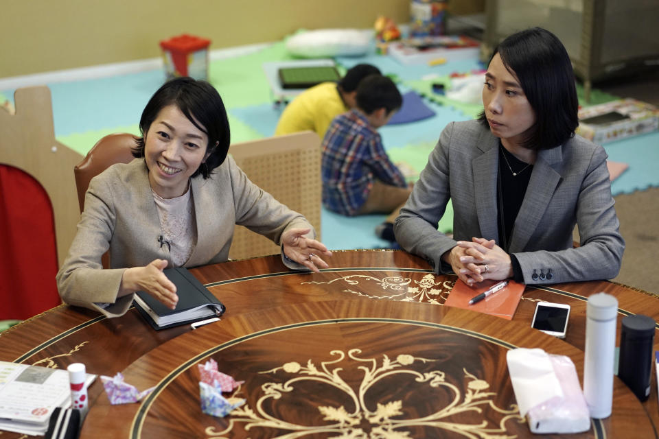 Keiko Kobayashi, left, and Sachiko Aoki, both employees of a staffing services company Pasona Inc. work as their children entertain themselves behind at the company's headquarters Monday, March 2, 2020, in Tokyo. Many Japanese schools were shut down Monday and spring holidays began unexpectedly early for children as part of a government-led measure to prevent further escalation of the coronavirus. The measure is a big burden and a headache for working mothers, especially those with small children or disabilities. (AP Photo/Eugene Hoshiko)