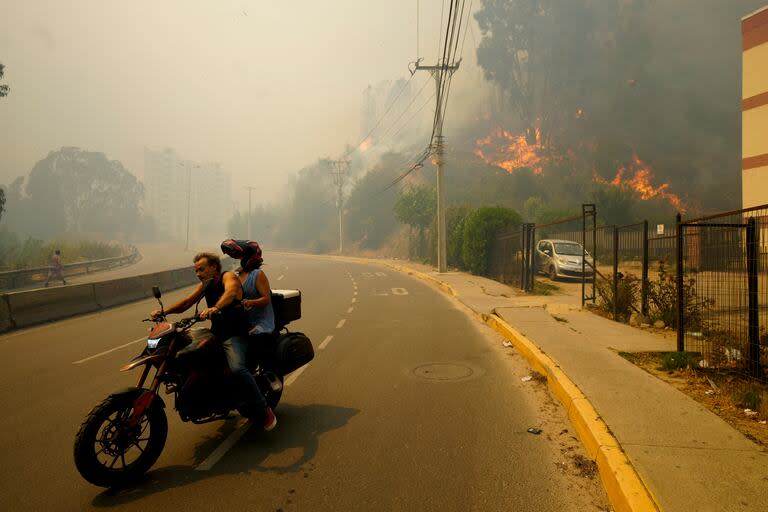 Residentes evacúan en una motocicleta entre incendios forestales en Viña del Mar, Chile, el 3 de febrero de 2024