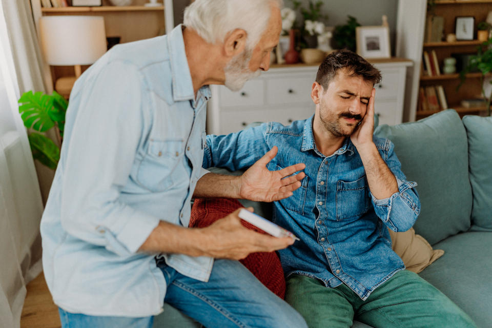 Older man comforting younger man sitting on couch, both in casual attire