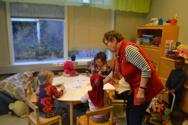 A communal grandmother helps a group of children sitting at a table draw pictures