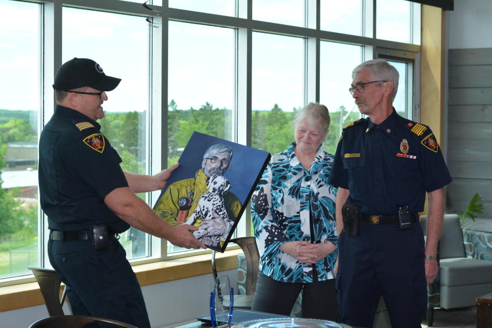 On behalf of the Woodstock Fire Department members, Ryan Gould presents the McLellans with a portrait of Chief McLellan and his Dalmatian pup, Ember, painted by artist Jennie Weeks.
