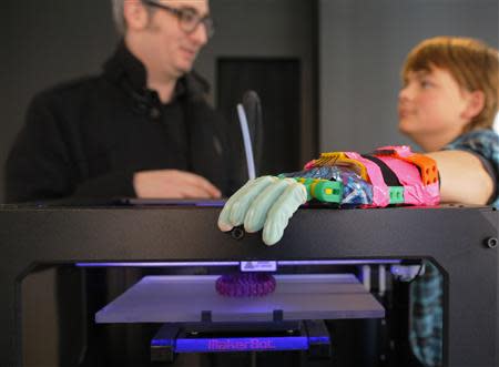 Twelve-year-old Leon McCarthy (R) rests his prosthetic hand on a MarkerBot Replicator 2 Desktop 3D Printer, while talking to the company's CEO Bre Pettis, at the new MakerBot store in Boston, Massachusetts November 21, 2013. REUTERS/Brian Snyder