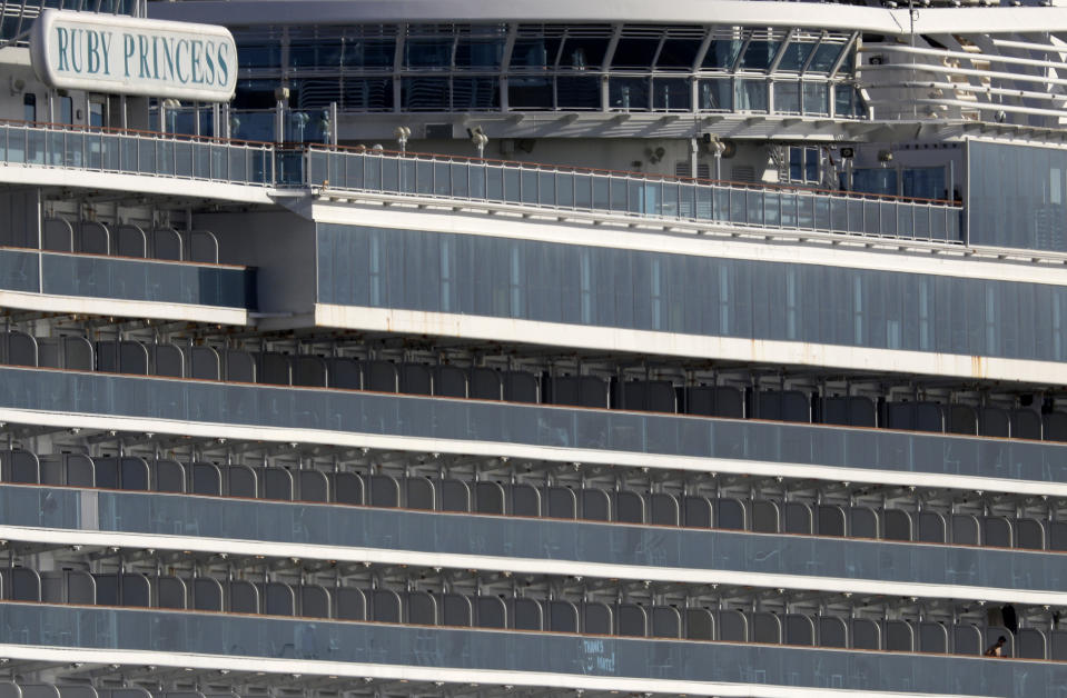 A person, bottom right, looks over the balcony of a cabin on the cruise ship Ruby Princess that is docked at Port Kembla as authorities prepare for the ship's departure in Wollongong, Thursday, April 23, 2020. The Ruby Princess has been ordered to leave Australia after disembarking passengers in Sydney in March that have tested positive for COVID-19. (AP Photo/Rick Rycroft)