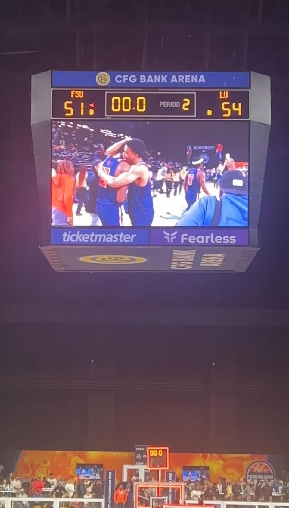 Scoreboard showing a basketball game result with players on the court celebrating