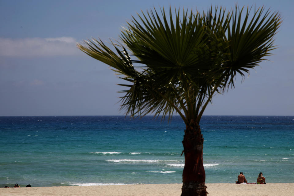 FILE - In this file image taken on Sunday, May 10 2020, sunbathers sit on an empty stretch of 'Landa' beach at the Cyprus seaside resort of Ayia Napa, a favorite among tourists. Cyprus' government Wednesday May 27, 2020, is pledging to cover all costs for anyone testing positive for the coronavirus while on vacation in the east Mediterranean island nation, covering the costs of lodging, food, drink and medication for COVID-19 patients and their families.(AP Photo/Petros Karadjias, FILE)