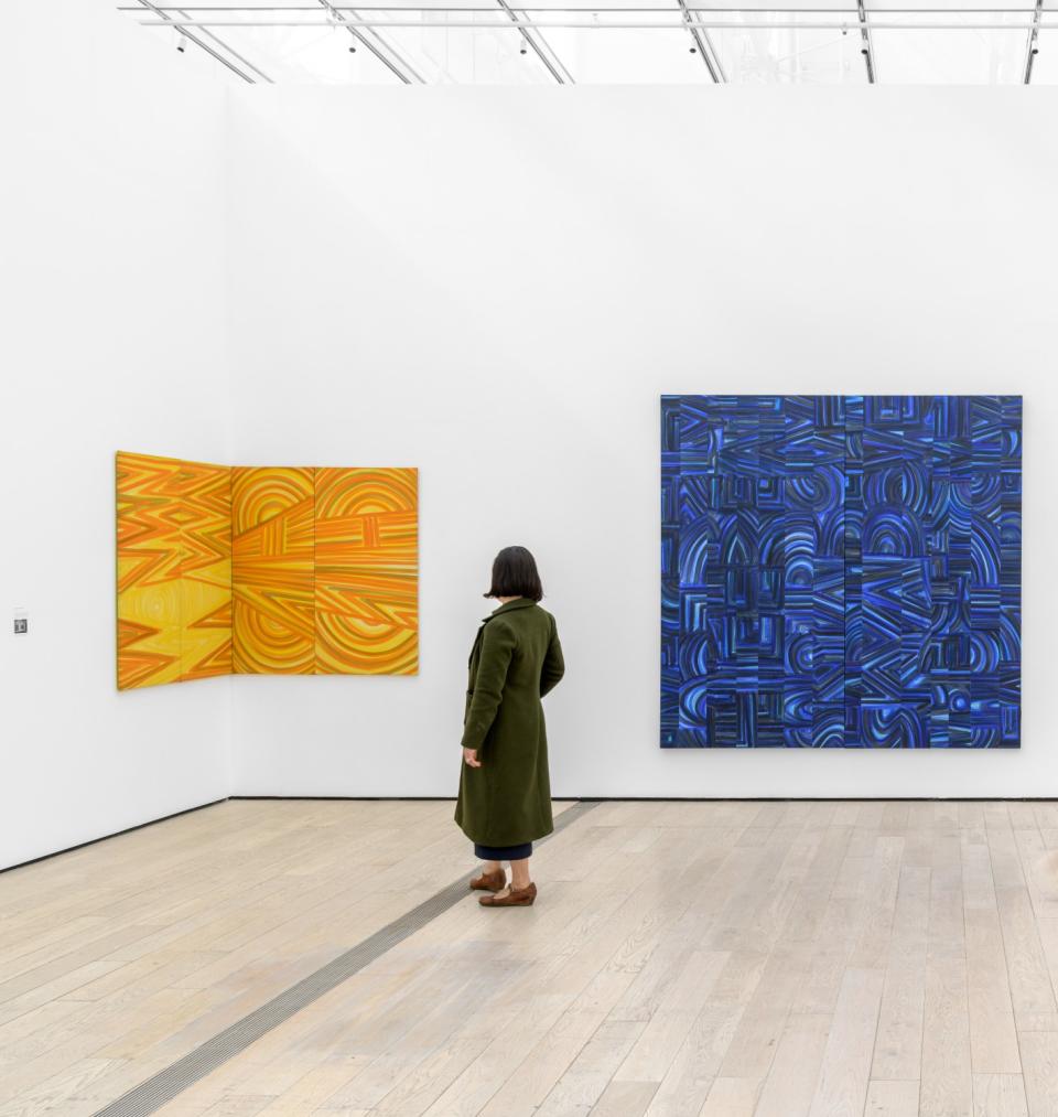 A viewer looks at a pair of abstract geometric canvases in shades of yellow and blue by Luchita Hurtado at LACMA.