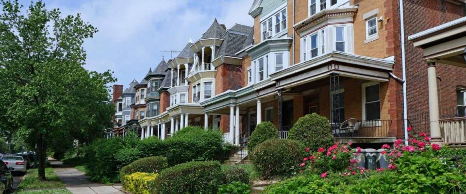 Row of large old brick houses with front porches and gardens