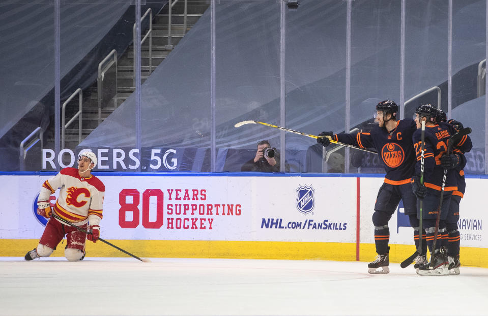 Edmonton Oilers' Connor McDavid (97), Tyson Barrie (22) and a teammate celebrate a goal as Calgary Flames' Mikael Backlund (11) gets up from the ice during the third period of an NHL hockey game Saturday, March 6, 2021, in Edmonton, Alberta. (Jason Franson/The Canadian Press via AP)