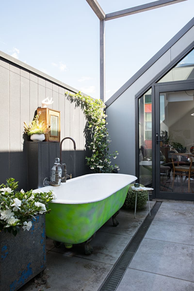 vintage green claw foot tub outside in sun room with plants