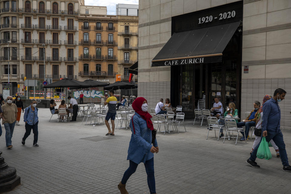 In this Monday, June 1, 2020 photo, people walk past a terrace bar with local customers in Barcelona downtown. Spain's strict lockdown that it is now scaling back managed to eventually control a COVID-19 outbreak that has claimed at least 27,000 lives. (AP Photo/Emilio Morenatti)