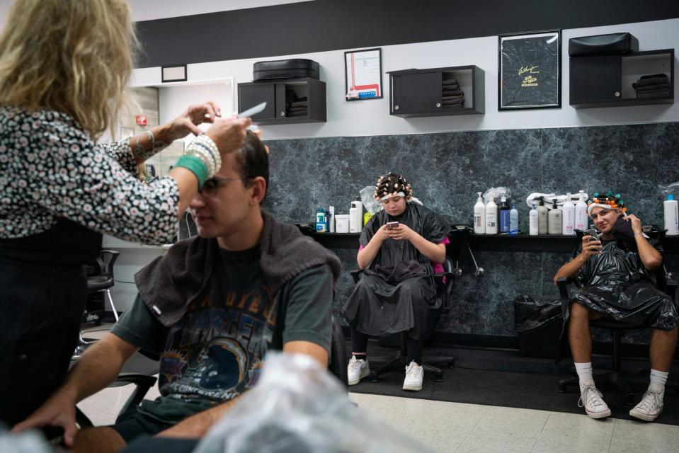 Nikki Elias-Porter, 68, of Dearborn, left, perms the hair of Owen Terechenok, 21, of Canton, as Emilie Nieves, 19, of Allen Park, and Jacob Terechenok, 16, wait for their hair to finish processing at Anthony's Hair Inc in Allen Park on July 25, 2023.