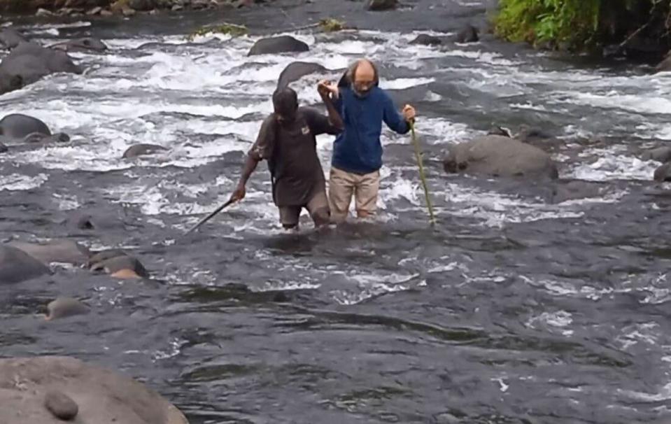 Dr Gianluca Grimalda crossing a stream with a local resident to reach a village in Papua New Guinea (Gianluca Grimalda)