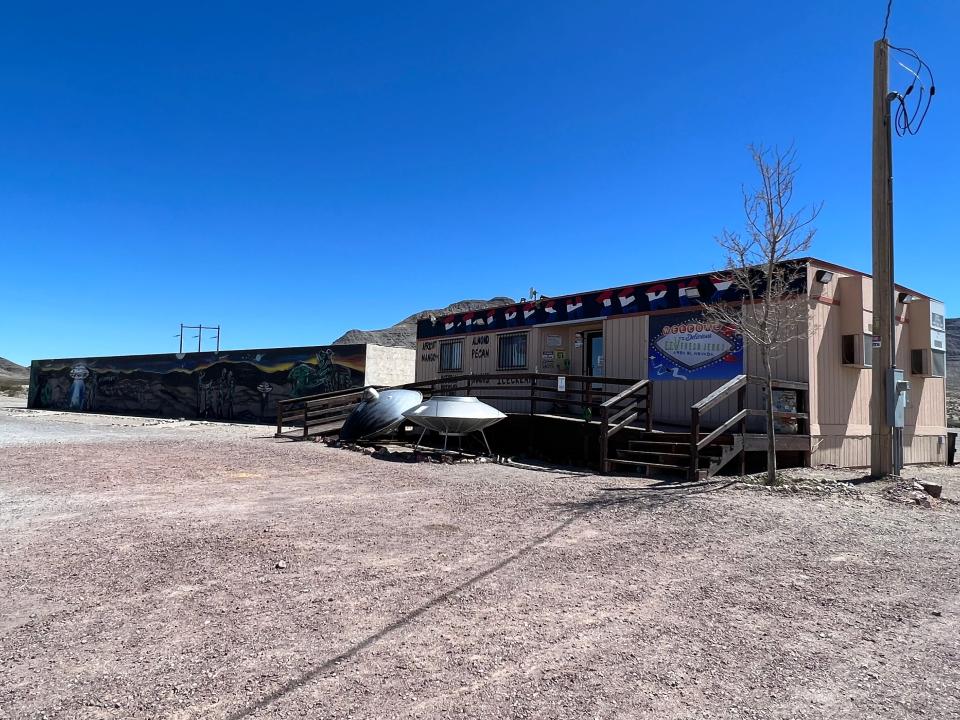 A building with a sign that says "E.T. Fresh Jerky." In front of the building are two silver flying saucers, and to the left is a long mural.