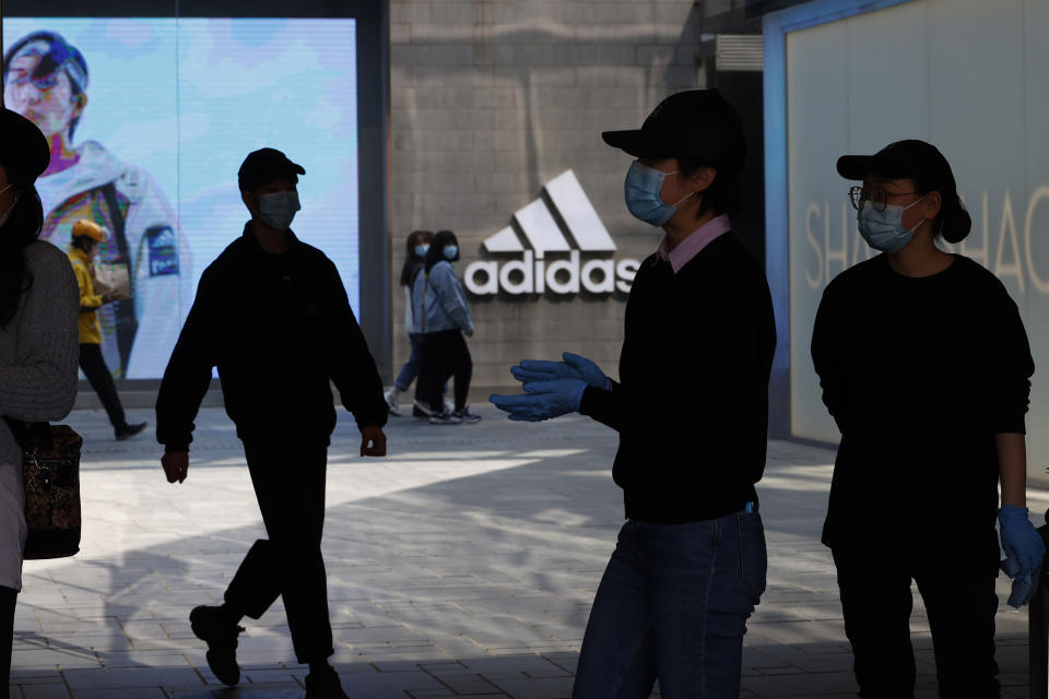 Workers and visitors stand near an Adidas store in Beijing on Thursday, March 25, 2021. China's ruling Communist Party is lashing out at H&M and other clothing and footwear brands as it retaliates for Western sanctions imposed on Chinese officials accused of human rights abuses in the northwestern region of Xinjiang. (AP Photo/Ng Han Guan)