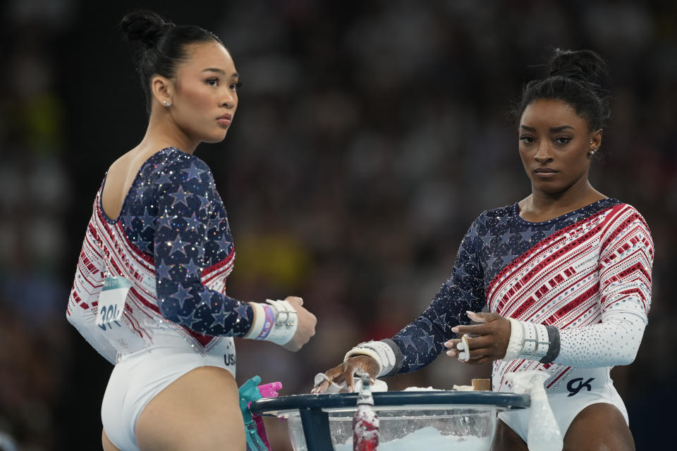 Simone Biles y Suni Lee, izquierda, de Estados Unidos, se preparan para actuar en las barras asimétricas durante la ronda final del equipo femenino de gimnasia artística en la Arena Bercy de los Juegos Olímpicos de verano de 2024, el martes 30 de julio de 2024, en París, Francia. (Foto AP/Charlie Riedel)