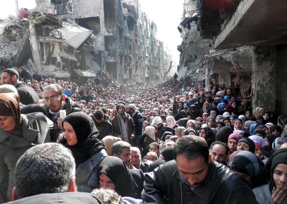 FILE -- In this Jan. 31, 2014, file photo, released by the United Nations Relief and Works Agency for Palestine Refugees in the Near East (UNRWA), shows residents of the besieged Palestinian camp of Yarmouk, queuing to receive food supplies, in Damascus, Syria. In one besieged neighborhood after another, weary rebels have turned over their weapons to the Syrian government in exchange for an easing of suffocating blockades that have prevented food, medicine and other staples from reaching civilians trapped inside. The government touts the truces as part of its program of “national reconciliation” to end Syria’s crisis, which has killed more than 140,000 people since March 2011. (AP Photo/UNRWA, File)