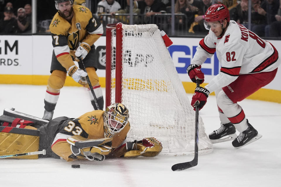 Vegas Golden Knights goalkeeper Adin Hill covers the puck beside Carolina Hurricanes center Jesperi Kotkaniemi (82) during the first period of an NHL hockey game Saturday, Feb. 17, 2024, in Las Vegas. (AP Photo/John Locher)