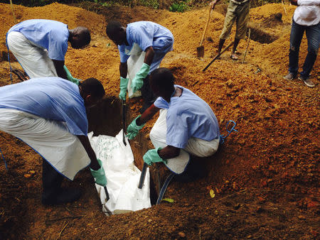 Volunteers lower a corpse, which is prepared with safe burial practices to ensure it does not pose a health risk to others and stop the chain of person-to-person transmission of Ebola, into a grave in Kailahun August 2, 2014. REUTERS/WHO/Tarik Jasarevic/Handout via Reuters