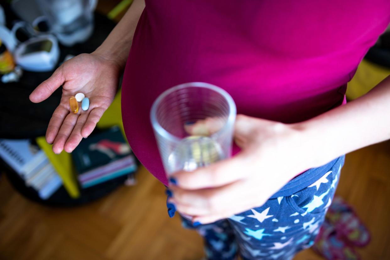 Beaitiful young pregnant woman holds vitamins pills and glass od water in her hand at home