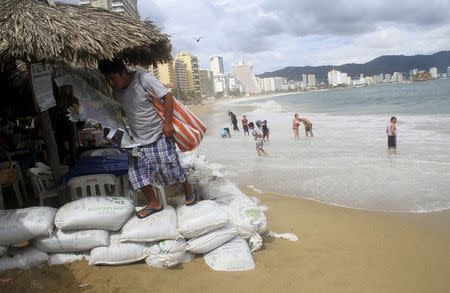 A vendor walks over sand bags placed by the personnel of a restaurant at a beach as dark clouds brought by the proximity of tropical storm Carlos are seen in Acapulco, June 12, 2015. REUTERS/Claudio Vargas